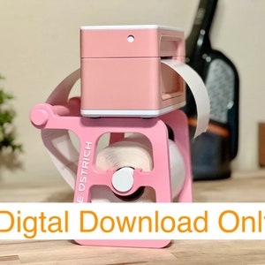 May include: A pink label printer with a roll of white labels on a pink stand. The printer has a white label dispenser and a white button on the top. The stand has the word "E-OSTRICH" printed on the side.