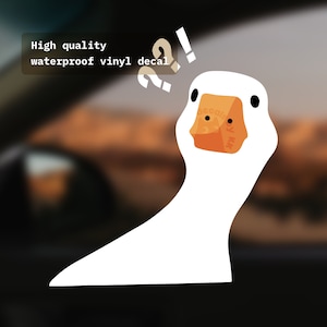 Peut inclure: Autocollant de canard blanc avec une expression confuse, avec des points d'interrogation et d'exclamation au-dessus de sa tête. L'autocollant est sur un fond flou d'une vitre de voiture. Le texte "High quality waterproof vinyl decal" est visible dans le coin supérieur gauche.