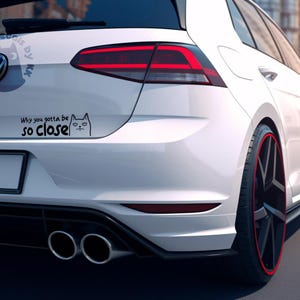 May include: White car with a black and white cat sticker on the rear bumper. The sticker says "Why you gotta be so close".