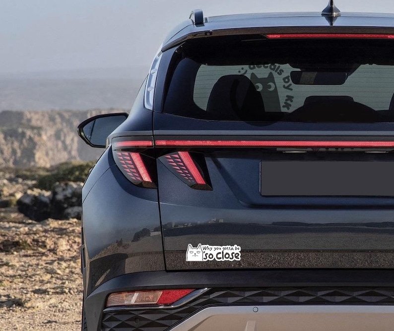 May include: A black SUV with a white cat sticker on the rear bumper that says "Why you gotta be so close".