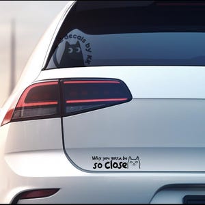 May include: White car with a black cat decal on the rear window and a black and white cat decal on the bumper that says "Why you gotta be so close".