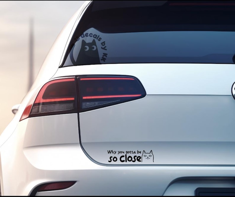 May include: White car with a black cat decal on the rear window and a black and white cat decal on the bumper that says "Why you gotta be so close".