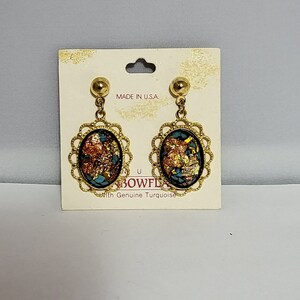 May include: A pair of gold tone earrings with oval shaped turquoise and gold leaf inlays. The earrings are on a white card with the text "Made in U.S.A." and "With Genuine Turquoise".