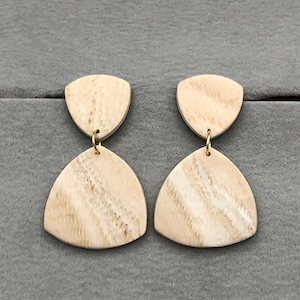 Może przedstawiać: Para kremowych kolczyków o geometrycznym wzorze. Każdy kolczyk ma mały, górny element w kształcie tarczy połączony ze sporym, trójkątnym dolnym elementem za pomocą złotego kółka. Kolczyki mają marmurkowy wzór.