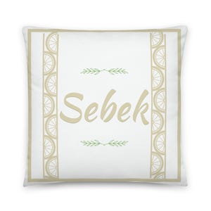 May include: Square decorative pillow with the name "Sebek" in a soft, light brown font. The pillow has a white background with a light brown border and vertical patterns of lemon slices. Small green leaf sprigs are above and below the name.