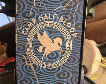 May include: A rectangular sign with a blue and black swirl pattern and white lightning bolts. The sign features the text "Camp Half-Blood" and a white Pegasus inside a circular border. A gold trident is also visible.