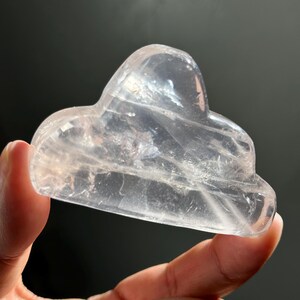May include: A clear, heart-shaped crystal with a smooth, polished surface. The crystal is carved into a unique shape, resembling a cloud or a mountain.