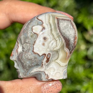 May include: A carved agate skull with a white, gray, and brown banded pattern. The skull is polished and has a smooth surface.