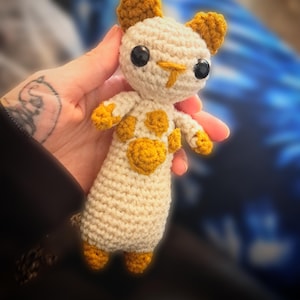 May include: A crocheted cat toy with a white body and yellow accents. The cat has a cute face with black eyes and a small nose.