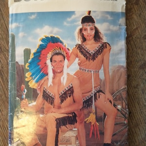 Op de afbeelding: Een vintage Butterick naaipatroonpakket, met een Native American kostuumontwerp. De omslag toont twee modellen in bruinachtige outfits met franjes en hoofdtooi, tegen een woestijnachtergrond. Het patroonnummer is 6853.