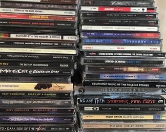 Op de afbeelding: Een verzameling vintage muziek-cd's die verticaal zijn gestapeld. De cd's bevatten een verscheidenheid aan artiesten, waaronder Led Zeppelin, Santana, The Who en Ozzy Osbourne. De cd's zijn in verschillende kleuren, waaronder zwart, zilver en goud.
