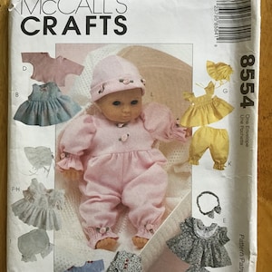 Könnte beinhalten: Ein Schnittmuster zum Nähen von Puppenkleidung. Das Schnittmuster enthält Anleitungen zum Nähen einer Vielzahl von Outfits, darunter ein Kleid, ein Overall, eine Mütze und ein Stirnband. Das Schnittmuster ist für eine Puppe mit einer Größe von etwa 45 cm geeignet. Das Schnittmuster stammt von McCall's Crafts und die Schnittmuster-Nummer lautet 8554.