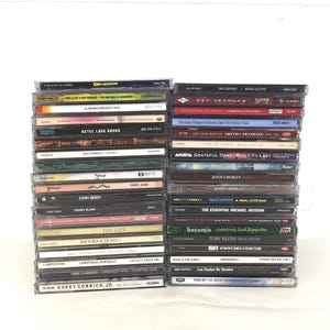 Puede incluir: Dos pilas de CD en estuches transparentes, que muestran portadas de álbumes y texto. Los títulos incluyen "Aztec Love Songs", "Bad Company" y "The Essential Michael Jackson". La imagen muestra una colección de álbumes de música.