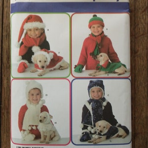 Könnte beinhalten: Simplicity Nähmuster Nummer 3973 zum Nähen von passenden Festtagsoutfits für ein Kind und einen Hund. Das Muster enthält vier verschiedene Designs: ein Weihnachtsmann-Outfit, ein Elfen-Outfit, ein Schneemann-Outfit und ein Winterwunderland-Outfit. Jedes Outfit beinhaltet eine Mütze, einen Schal und Fäustlinge für das Kind und eine passende Mütze und einen Schal für den Hund.