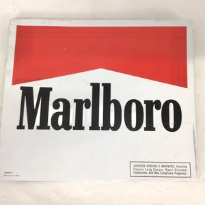 Op de afbeelding: Een wit bord met een rood bovenstuk en het woord "Marlboro" in vette zwarte letters. Het bord bevat een waarschuwing van de Surgeon General over roken.