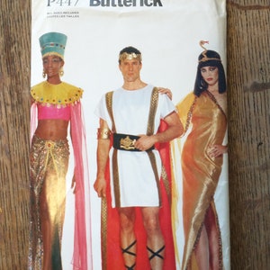 Puede incluir: Patrón de costura Butterick P447 con disfraces. La portada muestra tres figuras con atuendos del antiguo Egipto y Roma. Los disfraces incluyen telas doradas, rojas y blancas, con accesorios como tocados y cinturones. El patrón incluye todas las tallas.