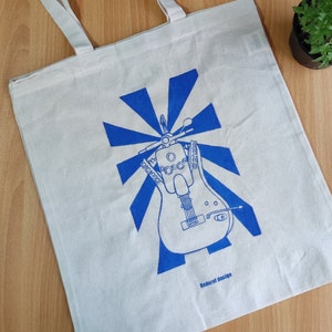 May include: A white tote bag with a blue and white graphic of a scooter and guitar with the text "Redort design".