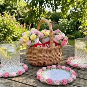 Peut inclure: Un panier en osier tressé rempli de petits bouquets de fleurs au crochet roses, jaunes et blancs, accompagné de trois dessous de verre ronds au crochet blancs avec des bords floraux roses et verts et deux verres texturés remplis de glaçons.