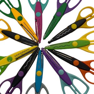 May include: A selection of decorative scissors in a circular arrangement. The scissors have handles in various colours such as yellow, green, purple, and orange, with black blades and decorative cutting edges. Each pair has a unique colour combination.