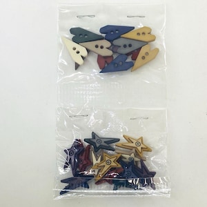 Puede incluir: Dos bolsas de plástico transparente llenas de botones de madera. Una bolsa contiene botones en forma de corazón en crema, azul marino, gris y burdeos. La otra bolsa tiene botones en forma de estrella en azul marino, burdeos, verde y beige.