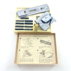 Puede incluir: Un kit de accesorios de máquina de coser para ojales vintage. El kit incluye varios componentes metálicos, una bandeja de plástico beige y una hoja de instrucciones impresa. La hoja de instrucciones tiene diagramas y texto sobre cómo usar el ojal.
