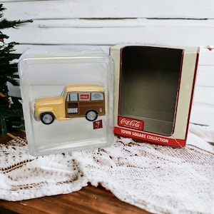 Peut inclure: Ornement de camion WKOK de la collection Coca-Cola Town Square, de couleur beige et marron, dans un étui en plastique transparent, à côté de sa boîte d'origine. Le camion porte le logo Coca-Cola et "NEWS WEATHER TONITE".