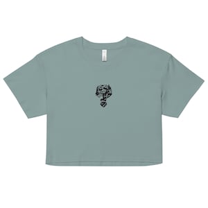 May include: A cropped, dusty blue t-shirt featuring a black graphic of a question mark filled with a landscape design. The shirt has short sleeves and a crew neck. The graphic is centered on the chest.
