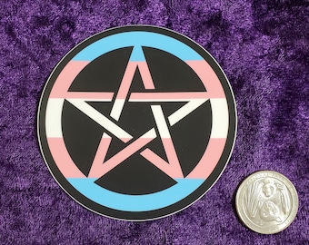 May include: A round sticker with a black pentagram inside a circle with a transgender pride flag design. The sticker is on a purple background.
