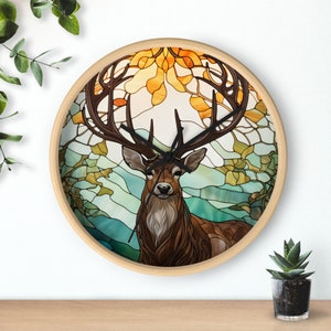 May include: Round wall clock with a stained-glass design featuring a majestic deer with large antlers. The clock face showcases a brown deer against a backdrop of autumn leaves in shades of orange, yellow, and green, set within a light wood frame.