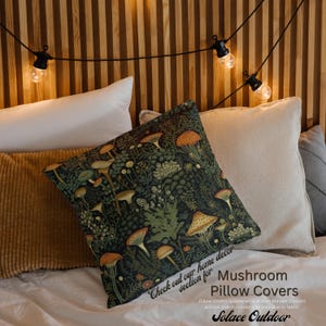 K&ouml;nnte beinhalten: Eine quadratische Kissenh&uuml;lle mit dunkelgr&uuml;nem Hintergrund und einem Muster aus orangefarbenen und beigefarbenen Pilzen und Bl&auml;ttern. Das Kissen liegt auf einem Bett mit anderen Kissen und einem h&ouml;lzernen Kopfteil. Auf dem Kissen steht "Check out our home decor section for Mushroom Pillow Covers".