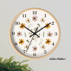 May include: Round wall clock with a light wood frame. The clock face is white, decorated with dried flowers in shades of yellow, pink, and white. Black hands and numerals mark the time. The clock is approximately 12 inches in diameter.