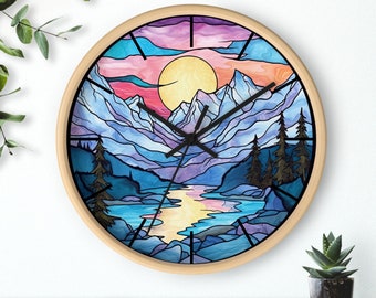 May include: A round wall clock with a light wood frame. The clock face features a colorful mountain landscape design with a sunset, river, and trees. The clock hands are black.