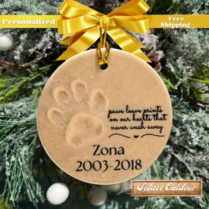 Puede incluir: Un adorno de cer&aacute;mica beige con una huella de pata y el texto "paws leave prints on our hearts that never wash away" y "Zona 2003-2018".
