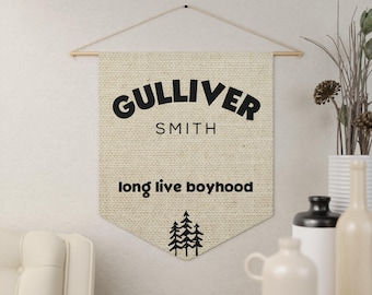 May include: A beige canvas wall tapestry with black text that reads "GULLIVER SMITH long live boyhood" and a black silhouette of pine trees.
