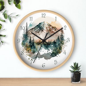 May include: A round wooden framed clock with a white face and black hands. The clock face features a watercolor painting of a mountain range with trees and a sunset sky. The numbers 1 through 12 are printed around the edge of the clock face.
