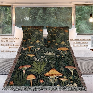 K&ouml;nnte beinhalten: Eine dunkelgr&uuml;ne Decke und zwei passende Kissen mit einem Pilzdesign. Die Decke ist gefranst und in drei Gr&ouml;&szlig;en erh&auml;ltlich: 81 x 145 cm, 127 x 152 cm und 152 x 203 cm. Die Kissen und die Decke zeigen ein sich wiederholendes Muster verschiedener Pilze.