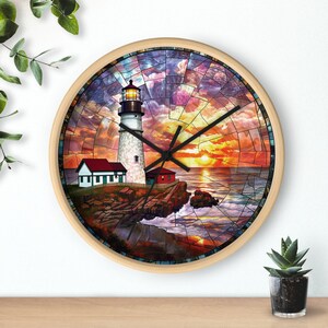 May include: A round clock with a stained glass design featuring a lighthouse, a small house, and a sunset over the ocean. The clock face is white with black hands.