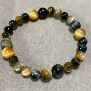 May include: A bracelet made of tiger's eye beads in shades of gold, blue, and black. The beads are round and have a smooth, polished finish.