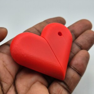Puede incluir: Un objeto rojo brillante en forma de coraz&oacute;n con un agujero en la parte superior. El coraz&oacute;n est&aacute; sostenido en la mano de una persona. El objeto parece estar hecho de pl&aacute;stico o un material similar.