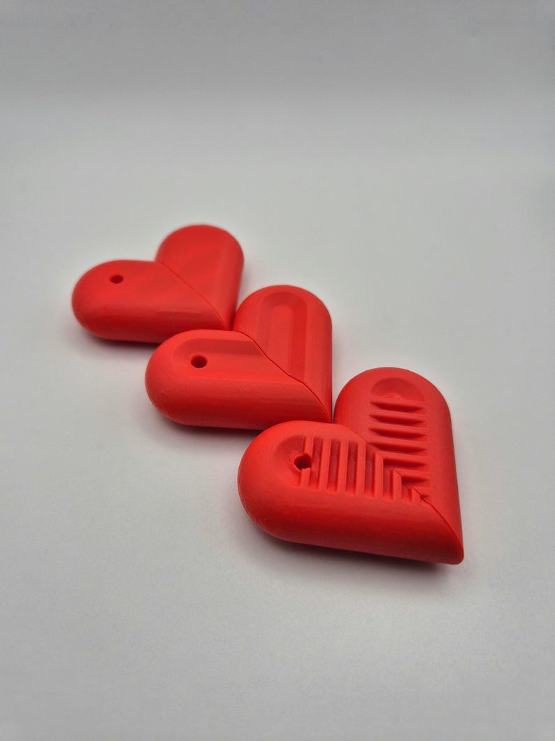 Puede incluir: Tres objetos rojos en forma de coraz&oacute;n con un dise&ntilde;o suave y redondeado. Cada coraz&oacute;n tiene un peque&ntilde;o agujero en la parte superior y uno tiene un patr&oacute;n texturizado en la mitad inferior. Los objetos est&aacute;n dispuestos sobre un fondo blanco.