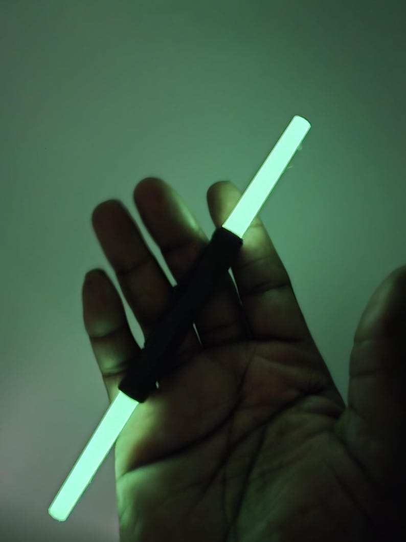 K&ouml;nnte beinhalten: Ein leuchtender, neongr&uuml;ner Stab mit einem schwarzen Griff. Der Stab wird in einer Hand vor einem gr&uuml;nen Hintergrund gehalten. Der neongr&uuml;ne Stab ist rechteckig und strahlt helles Licht aus.