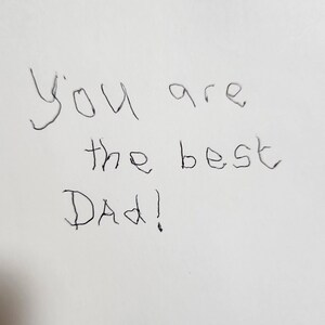 Op de afbeelding: Handgeschreven notitie op wit papier met de tekst "You are the best Dad!"