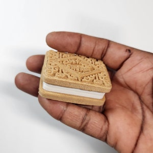 May include: A close-up of a chocolate sandwich cookie with a white cream filling. The cookie is held in a hand.