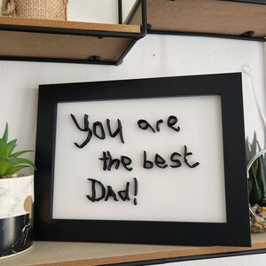 Op de afbeelding: Een zwart ingelijst beeld met een witte achtergrond en de woorden "You are the best Dad!" in zwart.