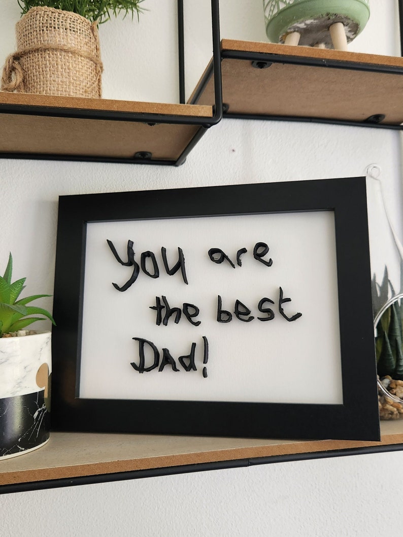 Op de afbeelding: Een zwart ingelijst beeld met een witte achtergrond en de woorden "You are the best Dad!" in zwart.