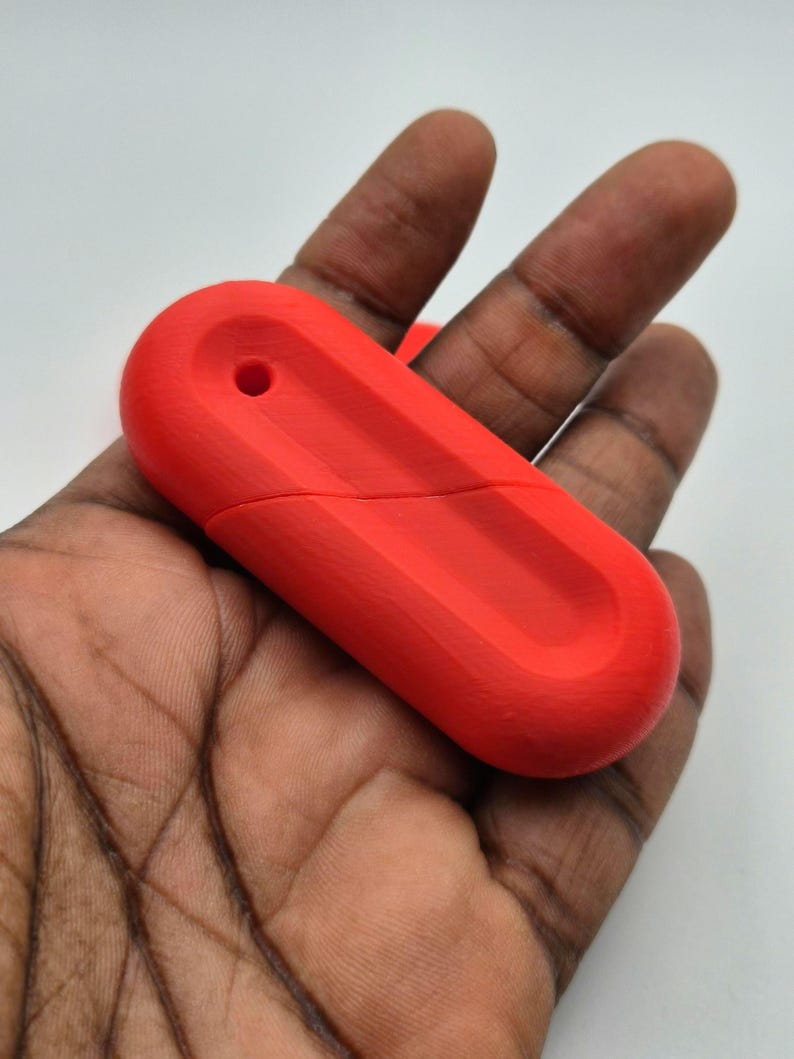 Puede incluir: Memoria USB roja brillante con forma rectangular redondeada. La unidad tiene un peque&ntilde;o agujero en un extremo y una superficie texturizada. El dispositivo se sostiene en una mano sobre un fondo blanco.