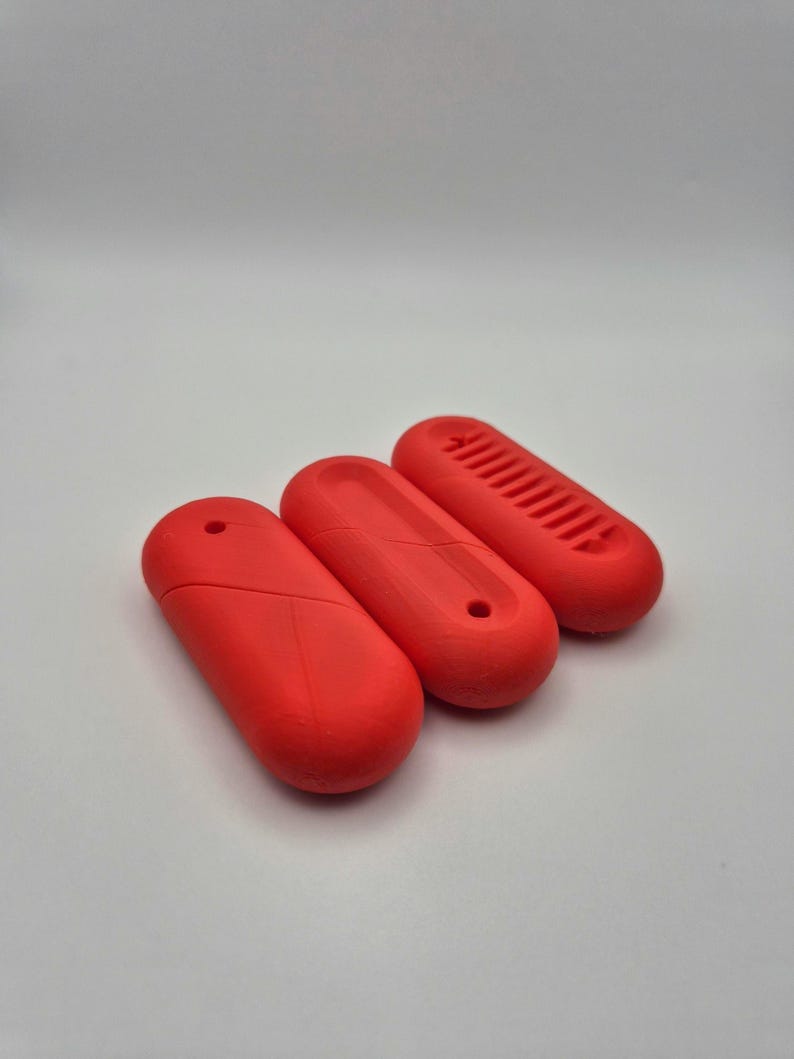 Puede incluir: Tres objetos oblongos de color rojo brillante. Los objetos tienen un dise&ntilde;o liso y redondeado con un peque&ntilde;o agujero en un extremo. Un objeto tiene una serie de l&iacute;neas paralelas en su superficie superior. Los objetos est&aacute;n dispuestos sobre un fondo blanco.