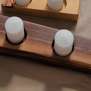 May include: A wooden candle holder with four slots for candles. The holder is made of dark wood with a natural grain pattern. There are four white candles in the slots.