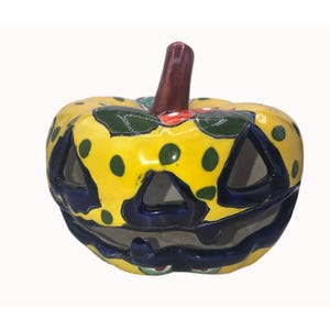 May include: A ceramic jack-o'-lantern with a yellow base, green polka dots, and dark blue accents. The pumpkin has triangular cut-out eyes and mouth, and a brown stem. A festive Halloween decoration.
