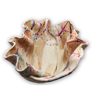 May include: A ceramic bowl with a ruffled edge and a white base. The bowl is decorated with splashes of pink, purple, and blue paint.
